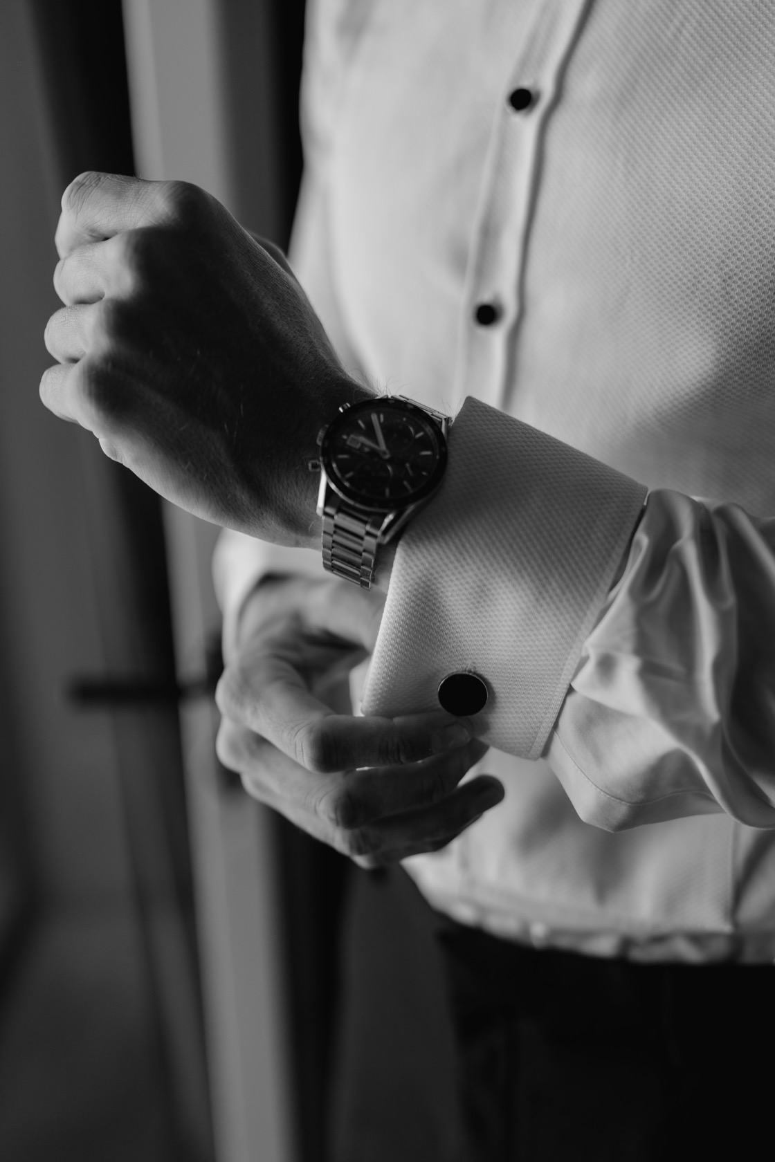 Groom fastening his cufflink, steel watch and white dress shirt, during wedding morning preparations