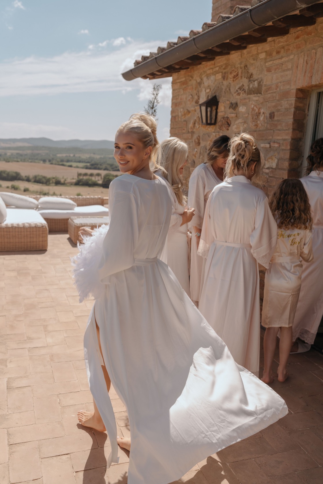 Bride in strapless white gown and cathedral veil and groom in white dinner jacket walking hand in hand along a cypress-lined drive at Conti di San Bonifacio Wine Resort, Tuscany.